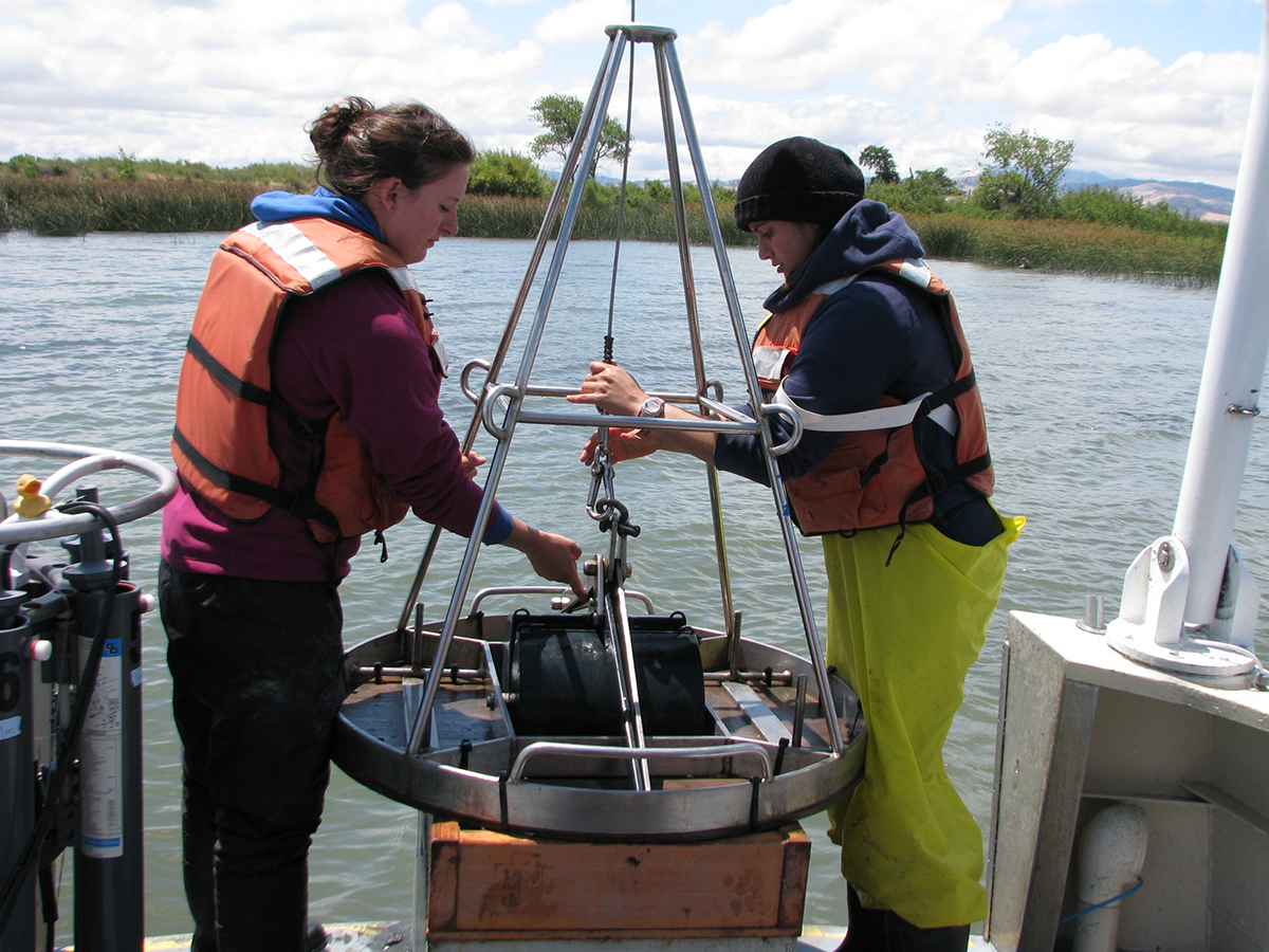two graduate students deploy sampling equipment off stern